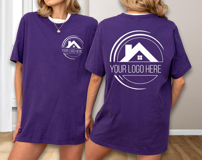 May include: A purple t-shirt with a white collar and a white logo on the front and back. The logo features a house silhouette inside a circular design, with the text "YOUR LOGO HERE" below. The shirt is a solid color.