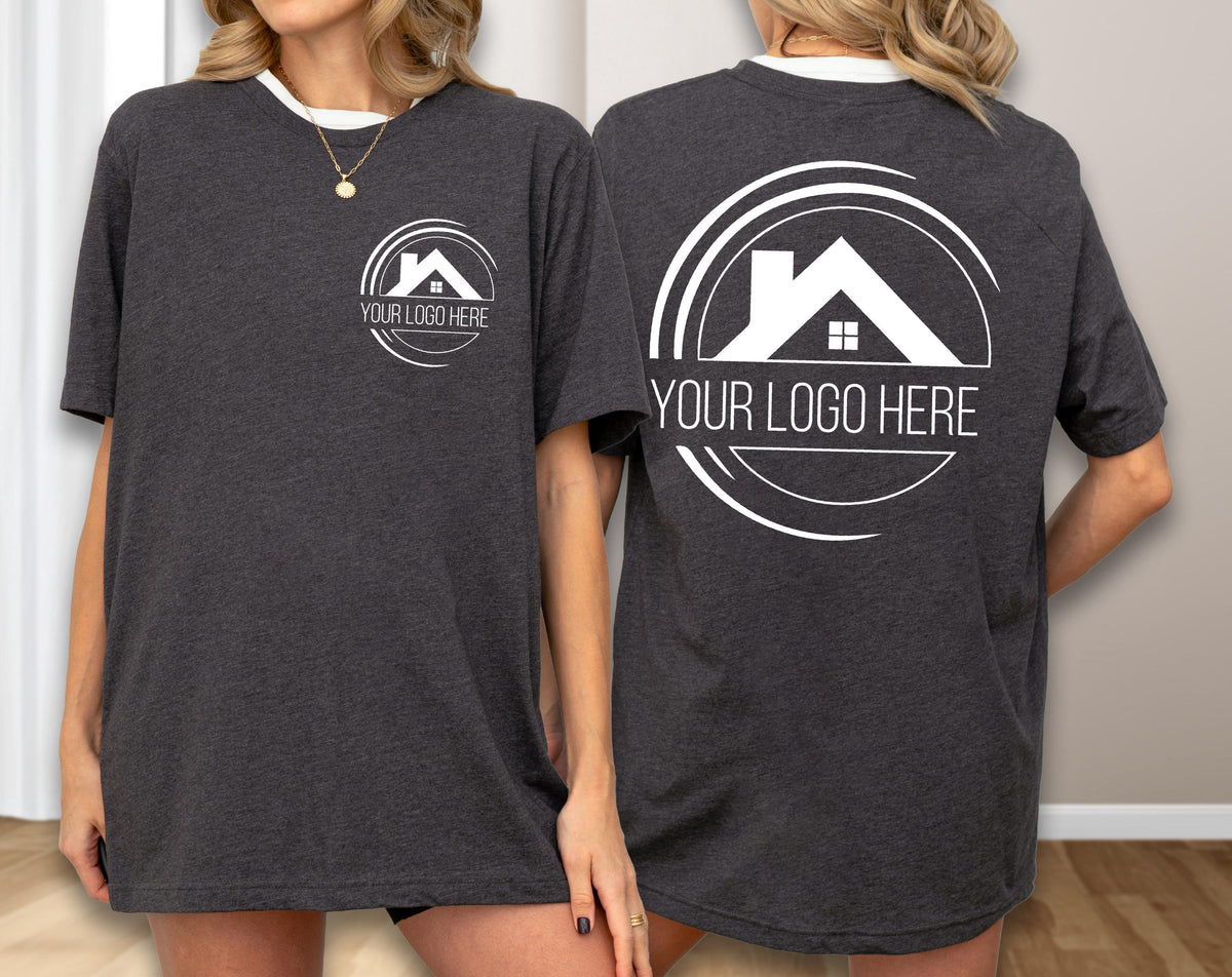 May include: Dark gray t-shirt with a white collar and a white logo featuring a house silhouette inside a circle. The text "YOUR LOGO HERE" is below the logo. The same logo is on the front and back of the shirt.
