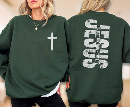 May include: Dark green sweatshirt with a white cross graphic on the front. The back of the sweatshirt features the word "JESUS" in large, distressed white letters, with the text "THE WAY THE TRUTH THE LIFE" stacked vertically above it. A casual, religious-themed garment.