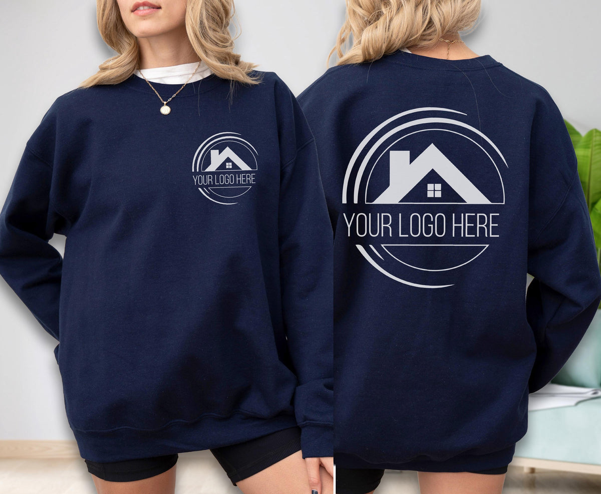 May include: Navy blue sweatshirt with a white logo on the front and back. The logo features a house silhouette inside a circular design, with the text "YOUR LOGO HERE". The sweatshirt is a casual garment.