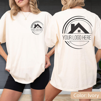 May include: Ivory-colored t-shirt with a black logo on the front and back. The logo features a house silhouette within a circular design, with the text "YOUR LOGO HERE" below. The shirt is a relaxed fit.