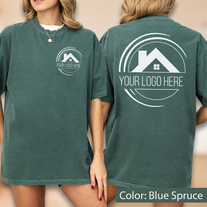 May include: Blue spruce-colored t-shirt with a white logo on the front and back. The logo features a house silhouette within a circular design, with the text "YOUR LOGO HERE". The shirt is a relaxed fit.