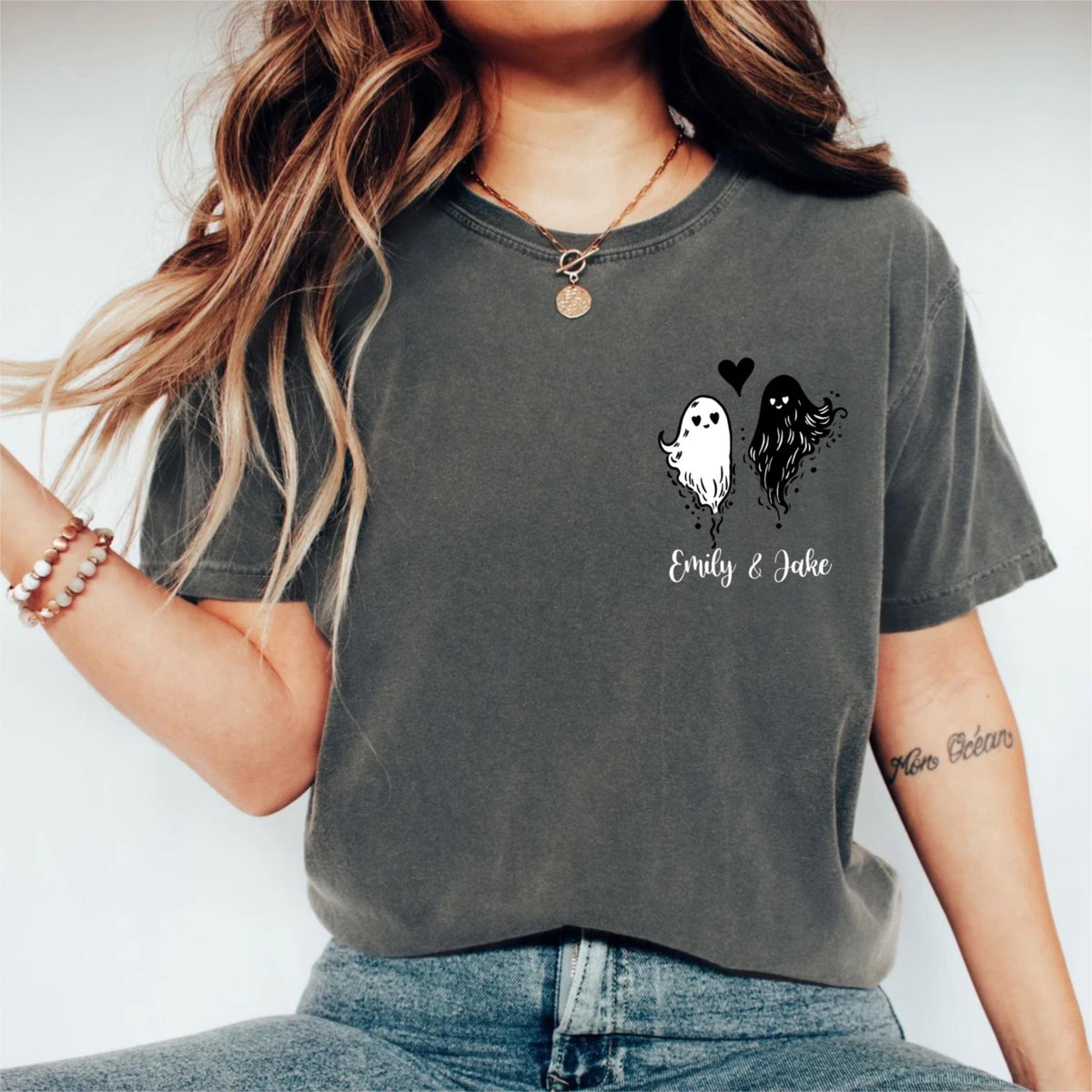 May include: A charcoal gray short-sleeve t-shirt featuring a graphic on the left chest area. The design includes a white ghost and a black ghost with a small black heart between them, with the text Emily & Jake printed below in white script.