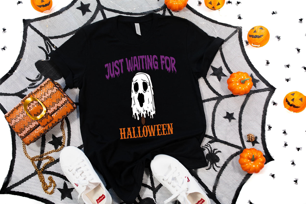 May include: Black t-shirt with the text "JUST WAITING FOR HALLOWEEN" and a white ghost graphic. The shirt is surrounded by Halloween decorations, including pumpkins, a spiderweb, a purse, and white sneakers.