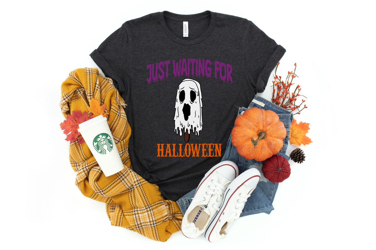 May include: Dark gray t-shirt with the text "Just Waiting For Halloween" and a ghost popsicle graphic. The shirt is surrounded by fall-themed items, including a pumpkin, scarf, and sneakers.