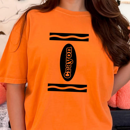 May include: A bright orange short-sleeve t-shirt featuring a black graphic design that mimics a crayon wrapper. The design includes two horizontal black wavy lines and a central black oval containing the word Crayon in orange lettering.