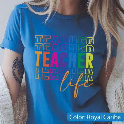 May include: A royal blue t-shirt featuring the word TEACHER repeated in a stacked, multi-colored block font, with the word life written in a cursive orange script below. The design uses vibrant shades of yellow, orange, pink, purple, and green.