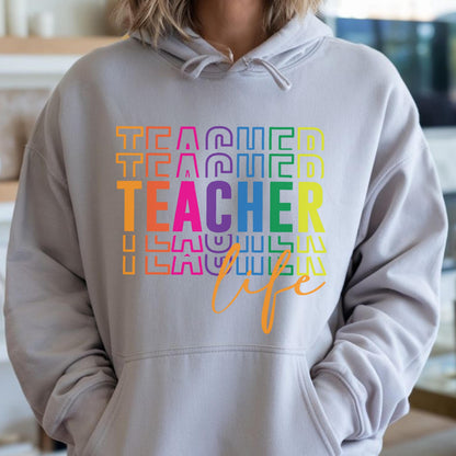 May include: A light gray hoodie with a front pocket and a drawstring hood. The front of the hoodie features the word "TEACHER" in rainbow colors, stacked vertically, with the word "life" in orange script below.