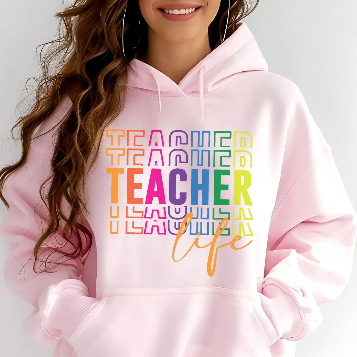 May include: A light pink hoodie with the words "TEACHER LIFE" in a rainbow gradient design. The word "TEACHER" is the largest and most prominent text on the front of the hoodie.
