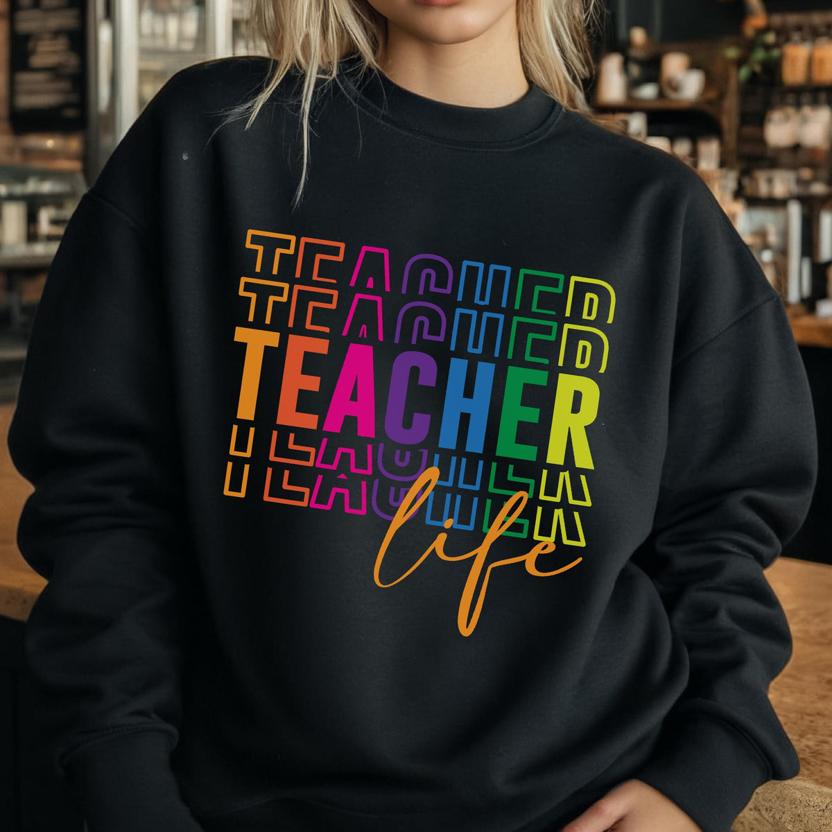 May include: Black sweatshirt with the word "TEACHER" in rainbow colors stacked vertically, with the word "life" in a cursive font below. The sweatshirt is a crew neck style.
