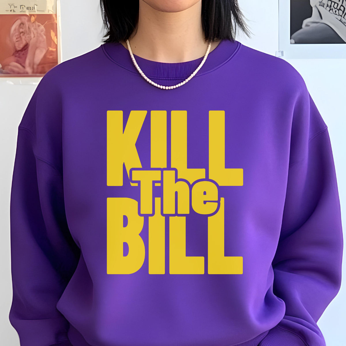 May include: A purple sweatshirt with the text "KILL The BILL" in yellow block letters. The sweatshirt has a crew neck and is worn with a white pearl necklace. The overall style is casual and bold, with a focus on the graphic text.