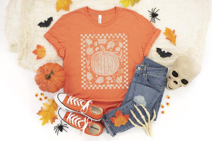 May include: Orange t-shirt with a pumpkin graphic, paired with blue jeans and orange sneakers. The image includes Halloween decorations like a skull, bats, and spiders, creating a festive autumn theme.