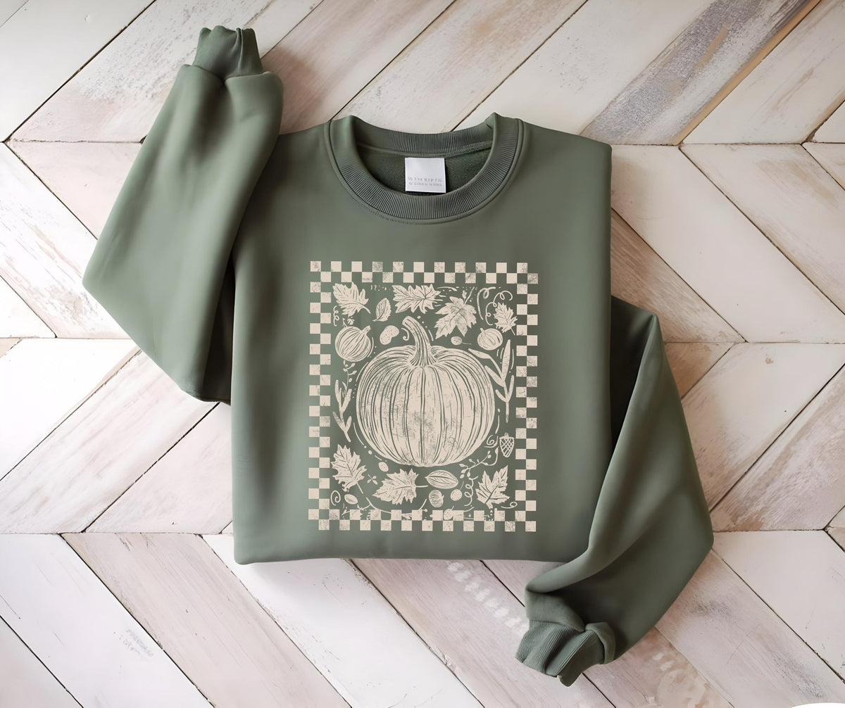 May include: Sage green sweatshirt featuring a cream-colored pumpkin graphic within a checkered border. The design includes leaves and other fall elements. The long-sleeved top is made of a soft material.