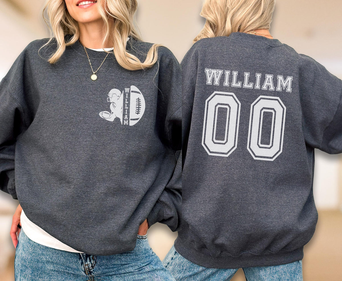 May include: A dark charcoal gray crewneck sweatshirt featuring a white graphic on the front left chest of a football player silhouette and a football with the name WILLIAM. The back displays the name WILLIAM and the number 00 in white block lettering.