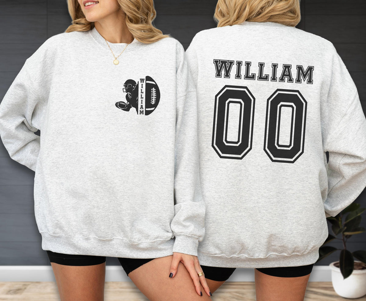 May include: A light gray crewneck sweatshirt featuring a black graphic on the left chest of a football player and a football with the name WILLIAM. The back displays the name WILLIAM in large black letters above the double zero jersey number 00.