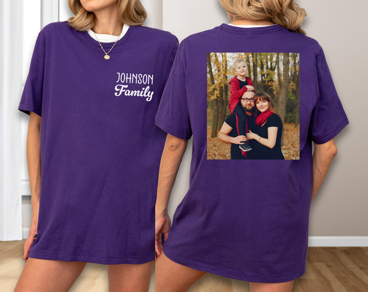 May include: A purple t-shirt with a white collar and the text "Johnson Family" in a script font. The back of the shirt features a family photo in a square frame. The photo shows a family of three in a forest setting.