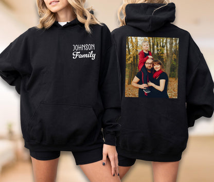 May include: Black hooded sweatshirt with a front pocket and the text "JOHNSON Family" in white script. The back of the sweatshirt features a family photo. A comfortable and personalized apparel item.