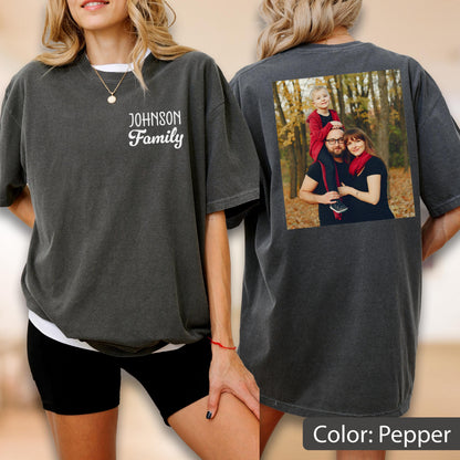May include: Pepper-colored t-shirt with a family photo on the back and the text "JOHNSON Family" on the front. The photo shows a family of three in a forest setting. The shirt is a relaxed fit.