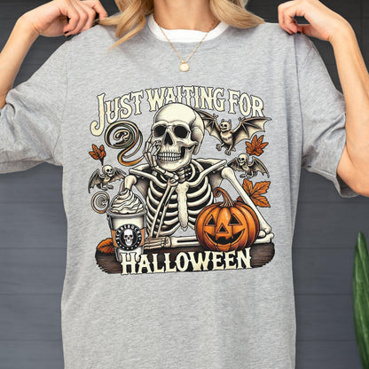 May include: Gray sweatshirt with a Halloween-themed graphic. The design features a skeleton, bats, a pumpkin, and a coffee cup. The text reads "Just Waiting For Halloween."
