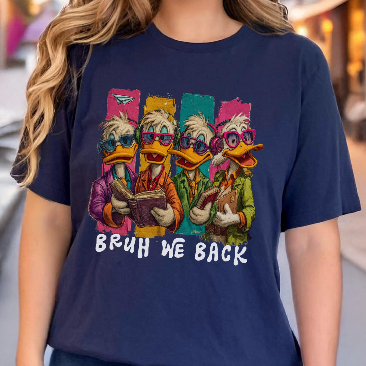 May include: Navy blue t-shirt featuring a cartoon illustration of four ducks wearing glasses and reading books. Each duck is set against a colorful vertical stripe. The text "BRUH WE BACK" is printed in white below the ducks.