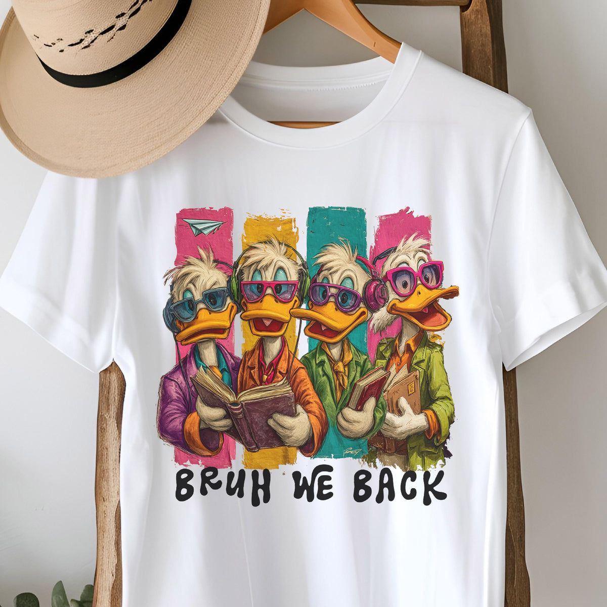 May include: White t-shirt featuring a cartoon illustration of four ducks wearing sunglasses and headphones, each holding a book. The ducks are set against colorful vertical stripes. The text "BRUH WE BACK" is printed below the ducks.