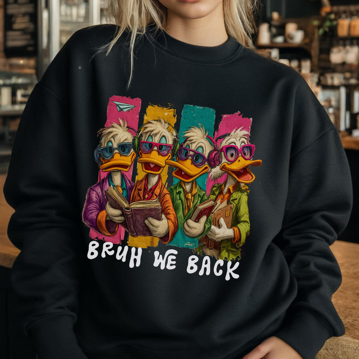 May include: Black sweatshirt featuring a cartoon illustration of four ducks wearing glasses and reading books. The ducks are set against colorful vertical stripes. The text "BRUH WE BACK" is printed in white below the ducks.