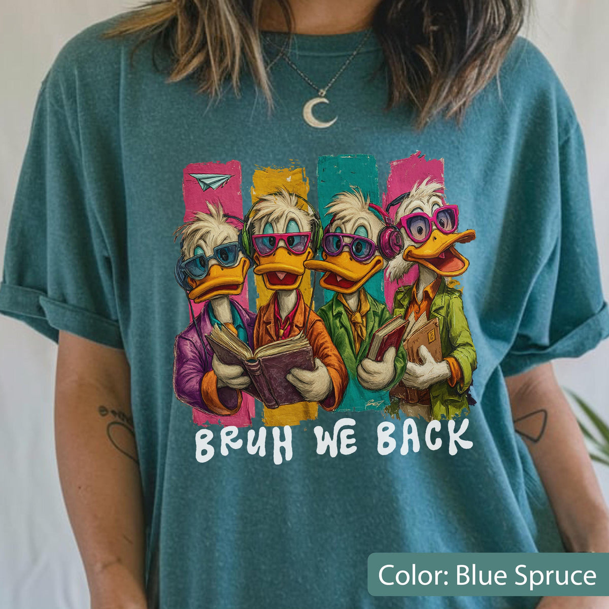 May include: Blue spruce t-shirt featuring a cartoon image of four ducks wearing glasses and headphones, each holding a book. The text "BRUH WE BACK" is printed in white below the ducks. The shirt has a relaxed fit.