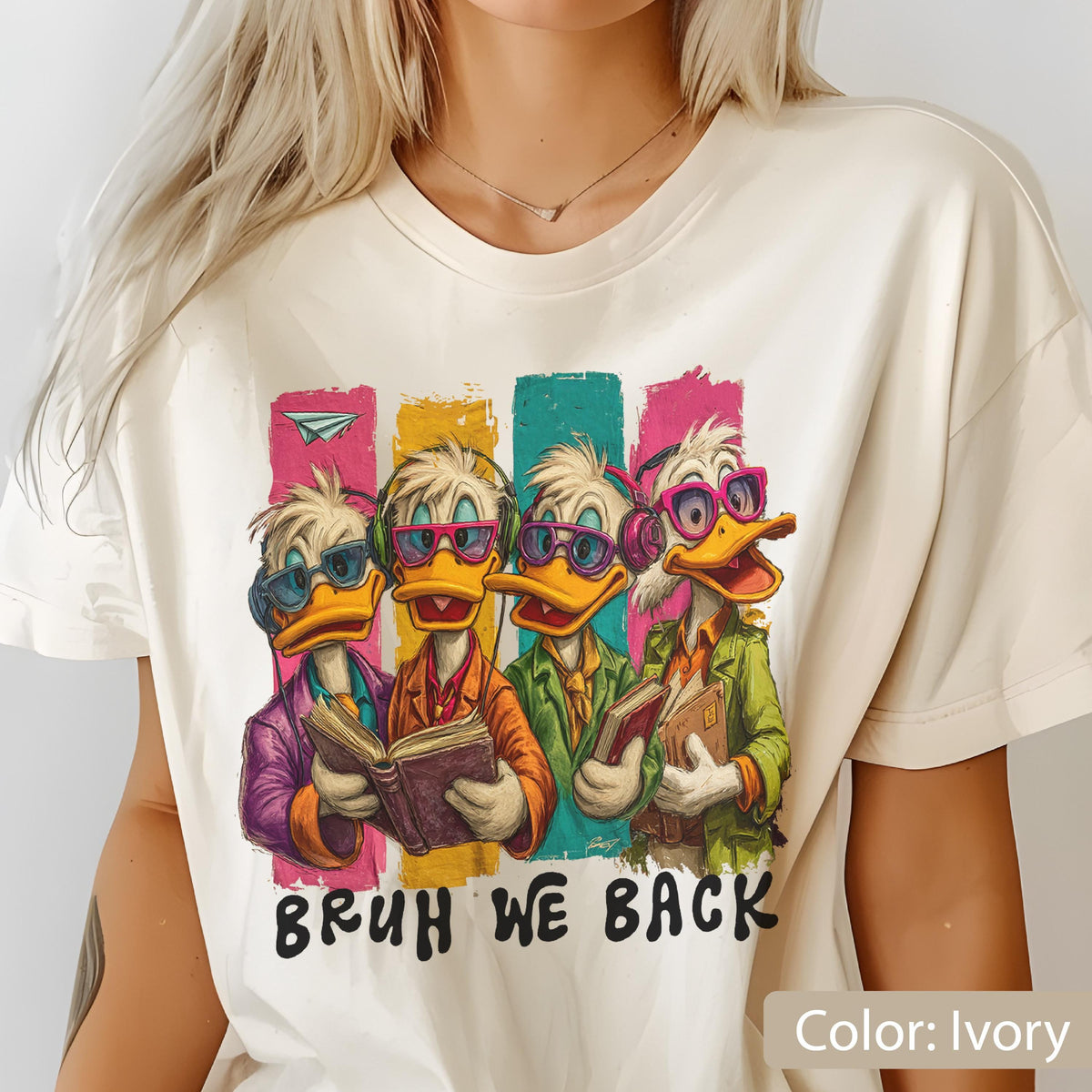 May include: Ivory-colored t-shirt featuring a cartoon illustration of four ducks wearing sunglasses and headphones, each holding a book. The ducks stand in front of colorful vertical stripes. The text "BRUH WE BACK" is printed below the ducks.