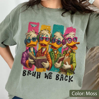 May include: Moss green t-shirt featuring a cartoon illustration of four ducks wearing glasses and holding books. The ducks are set against colorful vertical stripes. The text "BRUH WE BACK" is printed below the illustration.