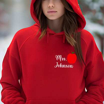 May include: A red hooded sweatshirt with the text "Mrs. Johnson" in white script, accompanied by a red apple graphic. The sweatshirt has a drawstring hood and a front pocket.