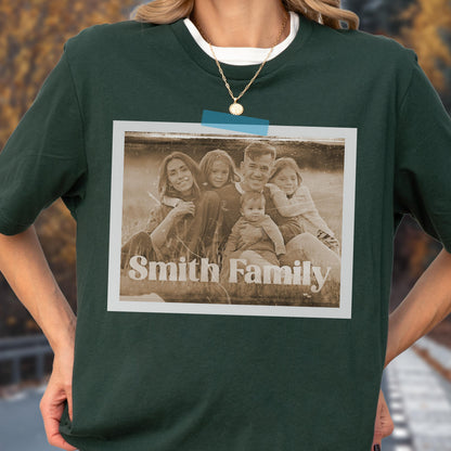 May include: Dark green t-shirt with a sepia-toned family photo attached with blue tape. The photo features a family of five with the words "Smith Family" printed at the bottom. The shirt has a white crew neck.