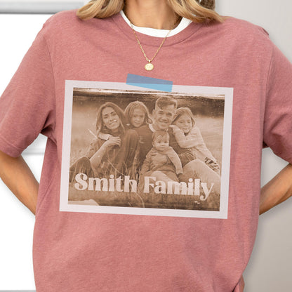 May include: A dusty rose t-shirt featuring a family photo with the text "Smith Family." The photo is a sepia tone and is taped to the shirt with blue tape. The shirt has a white crew neck collar.