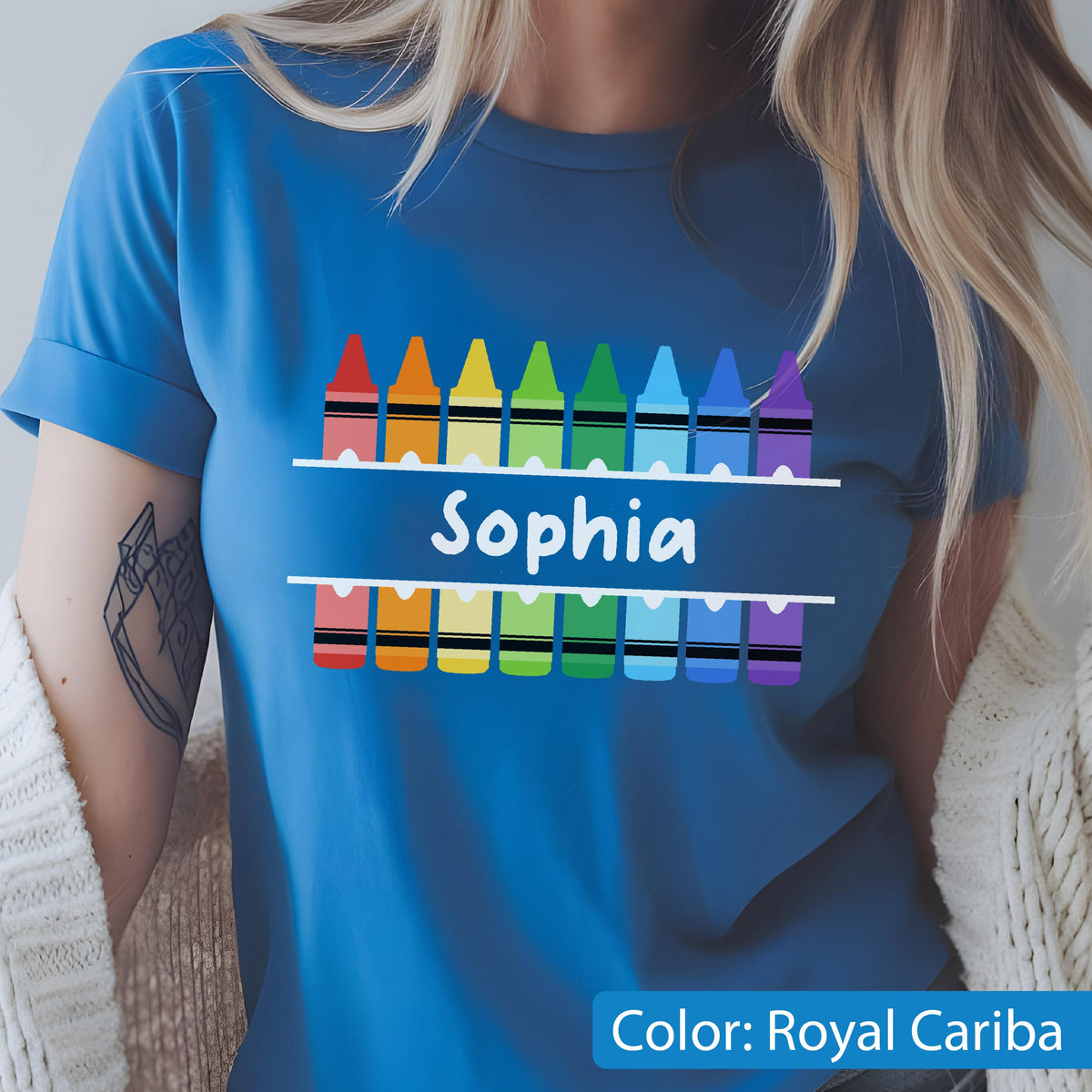 May include: Royal Cariba blue t-shirt featuring a row of colorful crayons above and below the name "Sophia" in white. The crayons are in a rainbow of colors. The shirt has rolled-up sleeves.
