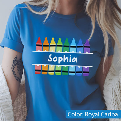 May include: Royal Cariba blue t-shirt featuring a row of colorful crayons above and below the name "Sophia" in white. The crayons are in a rainbow of colors. The shirt has rolled-up sleeves.