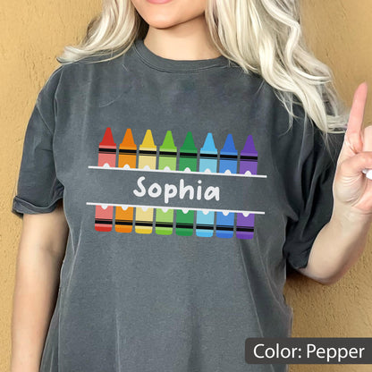 May include: Pepper-colored t-shirt featuring a colorful crayon design above and below the name "Sophia" in white. The crayons are arranged in a rainbow pattern. The shirt is a comfortable, casual style.