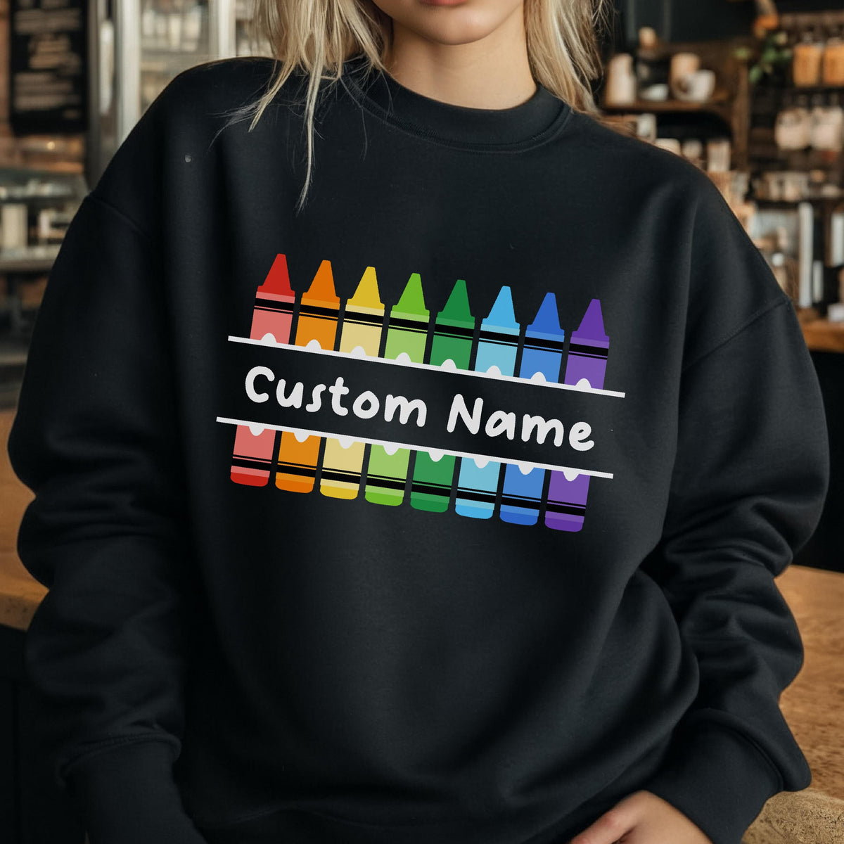 May include: Black sweatshirt featuring a colorful crayon design. The design includes a row of crayons in various colors above and below the text "Custom Name" in white. The sweatshirt is a comfortable, casual style.