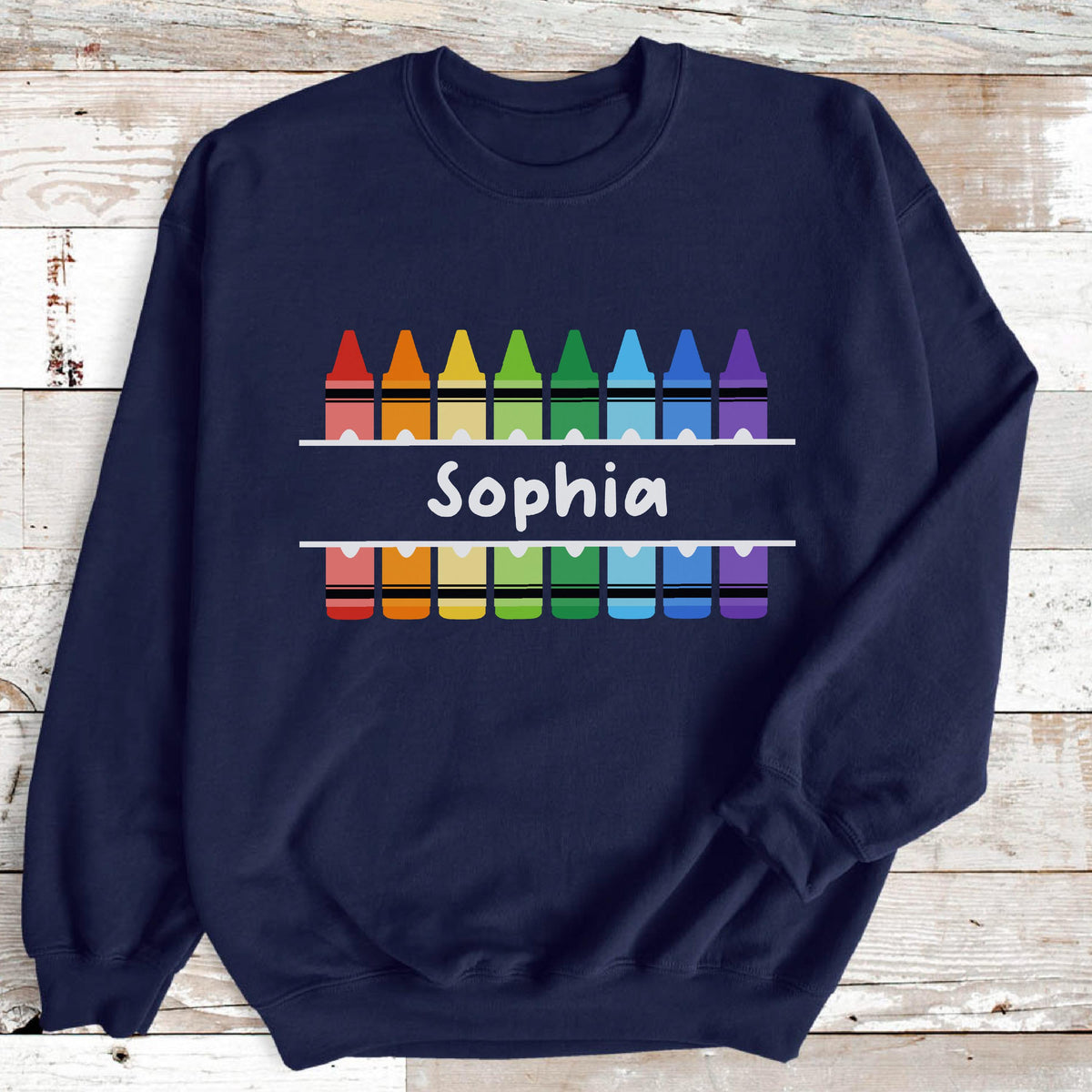 May include: Navy blue sweatshirt featuring a colorful crayon design. The design includes a row of crayons above and below the name "Sophia" in white, with a rainbow of colors. The sweatshirt is a comfortable, casual garment.