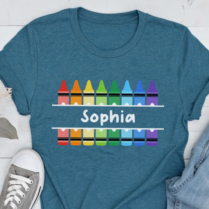 May include: Teal t-shirt featuring a colorful crayon design with the name "Sophia" in white. The design includes a row of crayons above and below the name, each in a different color.