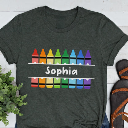 May include: Dark gray t-shirt with a colorful crayon design. The design includes a row of crayons above and below the name "Sophia" in white, with a rainbow of colors. The shirt is a casual style.