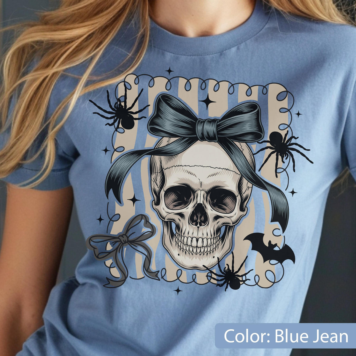 May include: Blue jean colored t-shirt featuring a skull with a dark blue bow, spiders, and a bat graphic. The design is framed by a striped background and the text "Color: Blue Jean".