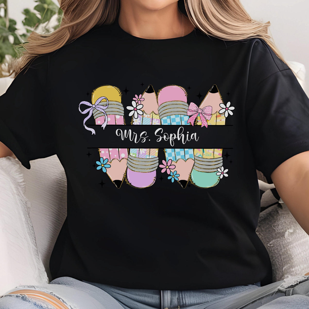 May include: Black t-shirt featuring a colorful pencil design with the text "Mrs. Sophia". The pencils have pastel colors, bows, and floral accents. A creative and personalized teacher gift.
