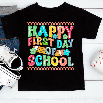 May include: A black short-sleeve t-shirt featuring a colorful graphic with the text "HAPPY FIRST DAY OF SCHOOL" in a bubbly, dotted font. The design includes a yellow pencil illustration, small teal flowers, and a checkered border pattern.