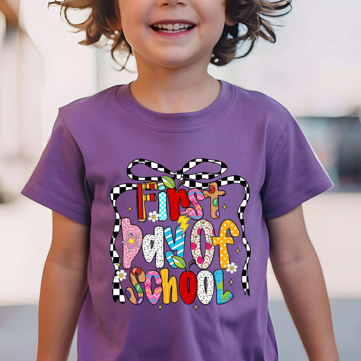 May include: A purple t-shirt with the text "First Day of School" in a colorful, playful design. The text is surrounded by a black and white checkered ribbon. The shirt is short-sleeved.