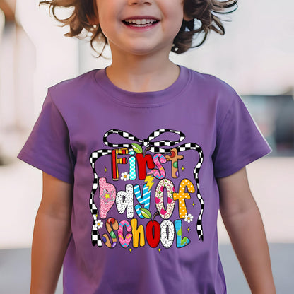 May include: A purple t-shirt with the text "First Day of School" in a colorful, playful design. The text is surrounded by a black and white checkered ribbon. The shirt is short-sleeved.