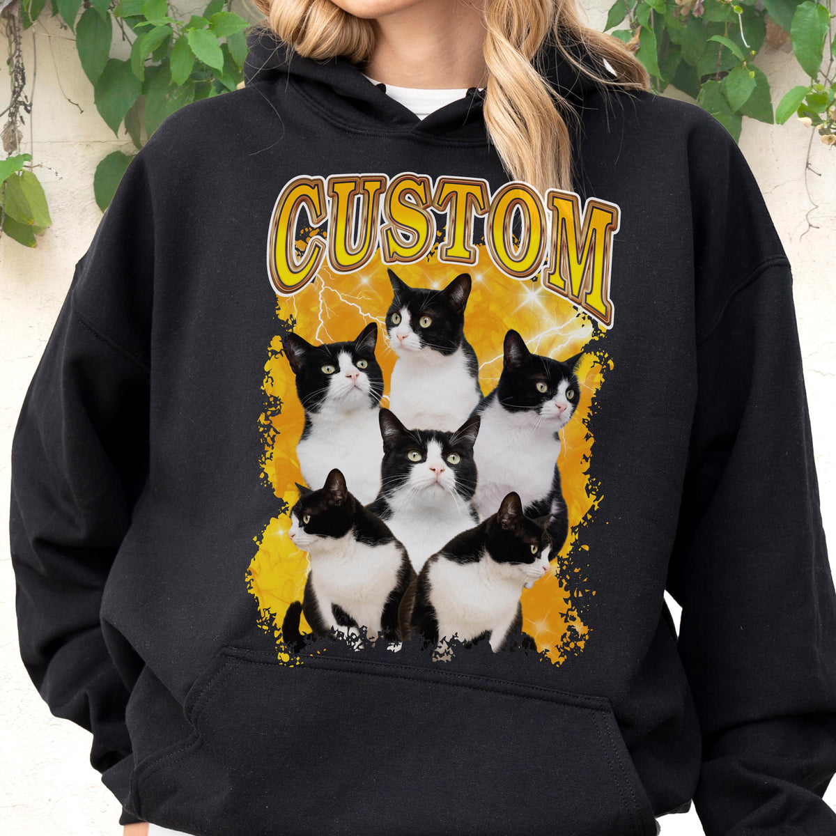 May include: Black hoodie featuring a graphic of six black and white cats on a yellow lightning bolt background. The word "CUSTOM" is printed above the cats in a yellow, distressed font. The hoodie has a drawstring hood and a front pocket.