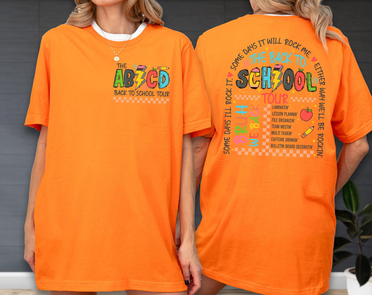 May include: Bright orange t-shirt with the text "THE AB7CD BACK TO SCHOOL TOUR" on the front. The back of the shirt features the text "SOME DAYS IT WILL ROCK ME, THE BACK TO SCHOOL TOUR" with school-related graphics. The shirt is a short-sleeved, casual style.