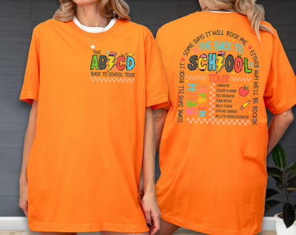 May include: Bright orange t-shirt with the text "THE AB7CD BACK TO SCHOOL TOUR" on the front. The back of the shirt features the text "SOME DAYS IT WILL ROCK ME, THE BACK TO SCHOOL TOUR" with school-related graphics. The shirt is a short-sleeved, casual style.