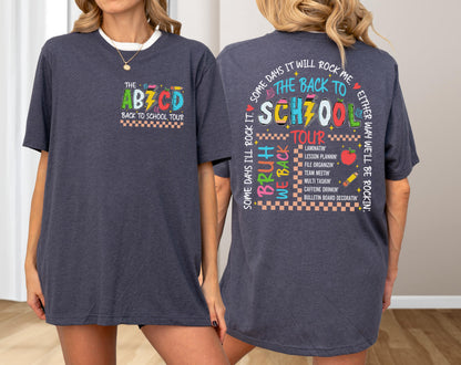 May include: Dark blue t-shirt with the text "THE ABZCD BACK TO SCHOOL TOUR" on the front pocket. The back of the shirt features the text "THE BACK TO SCHOOL TOUR" with a list of school-related activities. The shirt has a crew neck and short sleeves.