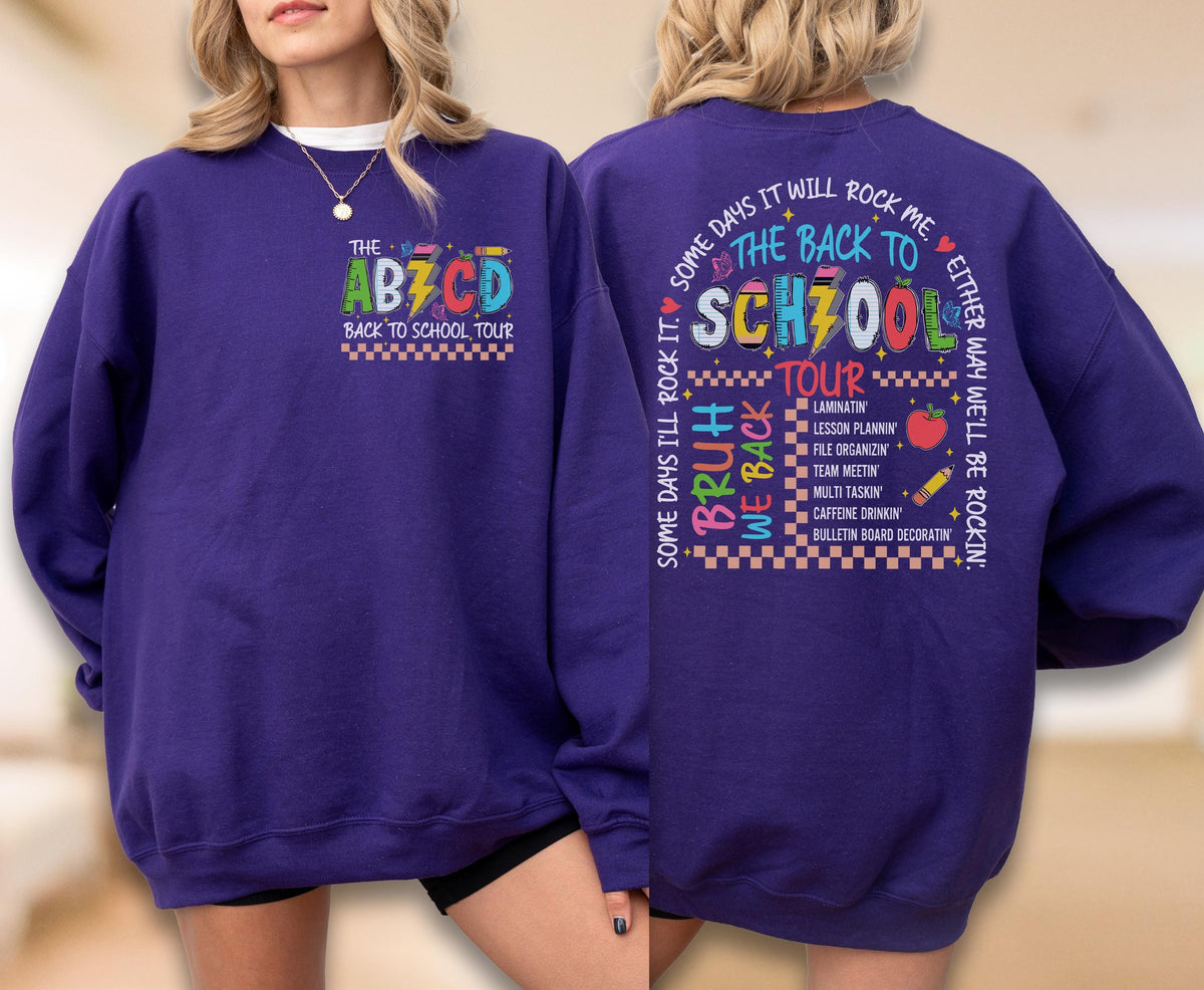 May include: A purple sweatshirt with the text "THE ABZCD BACK TO SCHOOL TOUR" on the front. The back of the sweatshirt has the text "THE BACK TO SCHOOL TOUR" with a list of school-related activities. The sweatshirt is a crew neck.