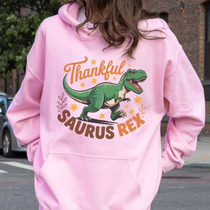 May include: Pink hooded sweatshirt with a graphic of a green Tyrannosaurus Rex dinosaur. The text on the sweatshirt reads "Thankful Saurus Rex" in brown and orange lettering, with fall leaves accents.